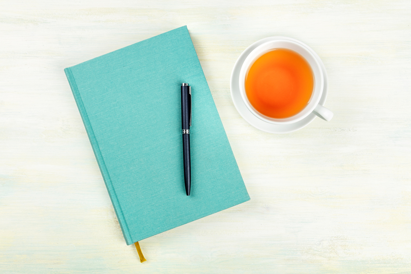 A teal blue journal with a pen and a cup of tea, shot from above, an elegant notebook on a light background with a place for text